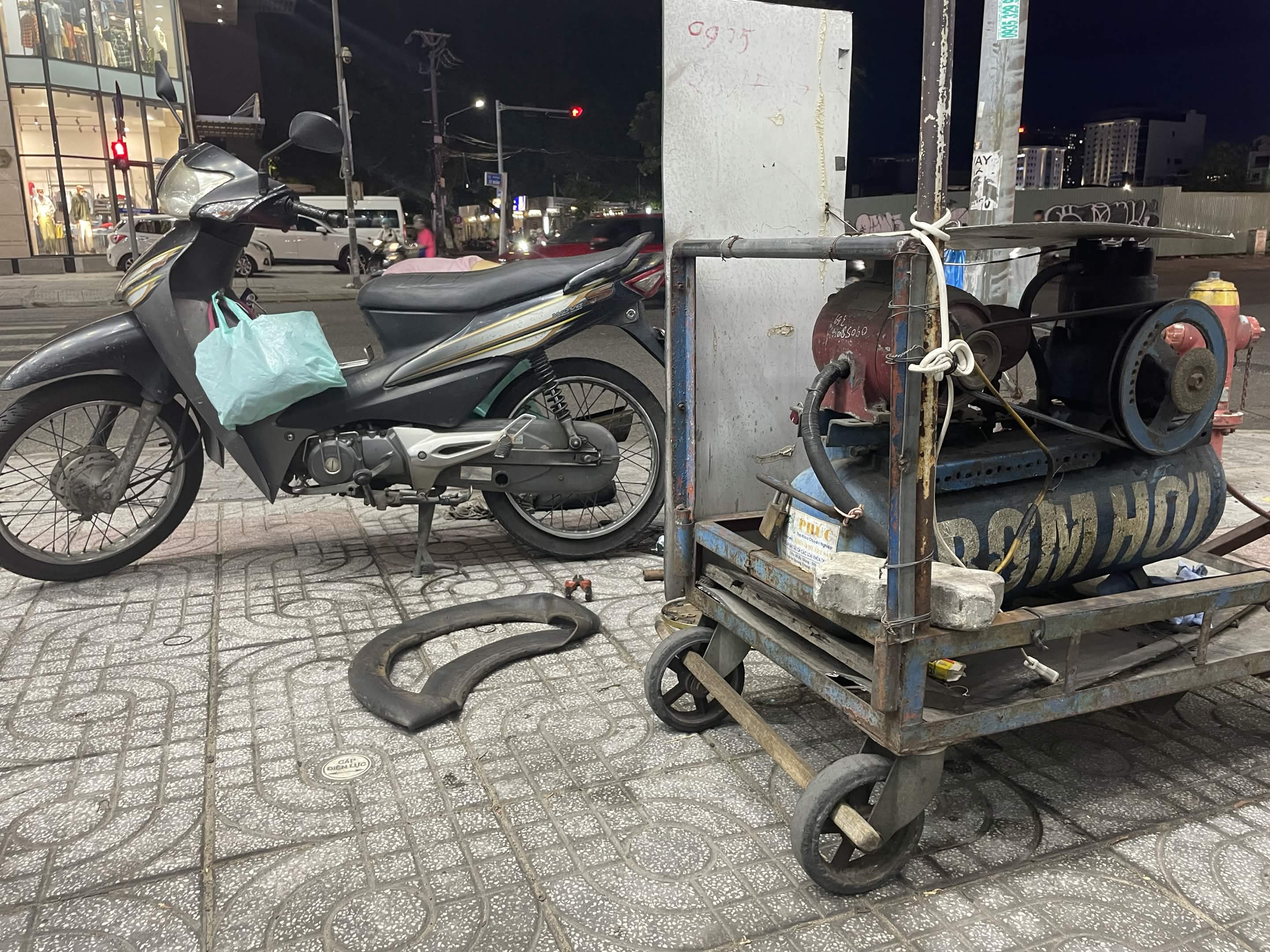 Chiếc xe máy bị lủng xăm đang được sửa bên lề đường vào buổi tối